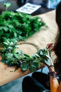A person making a wreath of green flowers and leaves 