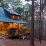 A wood frame cabin with large porch, lit up at nighttime.