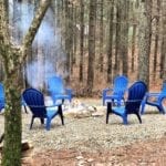 Fire pit surrounded by four bright blue metal chairs.
