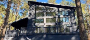 The exterior of the home, showing three floors of wide windows and a wraparound deck with railing.