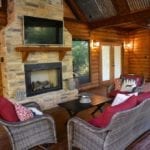 Wicker chairs with red cushions on the deck in front of a large fireplace.