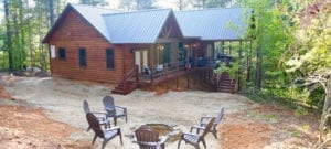 Exterior of the cabin, a log-style home with a large porch and stairs going up to it.