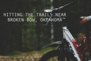 Close-up photo of a mountain bike's handlebars against a forest backdrop. Title: Hitting the trails in Broken Bow, Oklahoma.