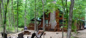 The exterior of Lukfata Creek Cabin, a two-story A-frame with large wraparound porch and surrounded by towering trees.