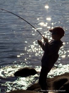 Boy fishing on lake bank at dusk.