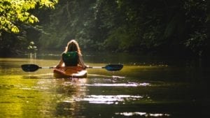 A woman paddling a canoe on the river on a sunny day.