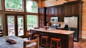The open kitchen featuring dark cabinets, a large island with stools and a glimpse of the large dining table.
