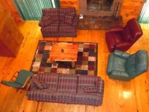 A view looking down on the living room with plaid covered sofas, leather chairs and stone fireplace.