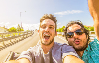 Two men taking a selfie in a car on the road.